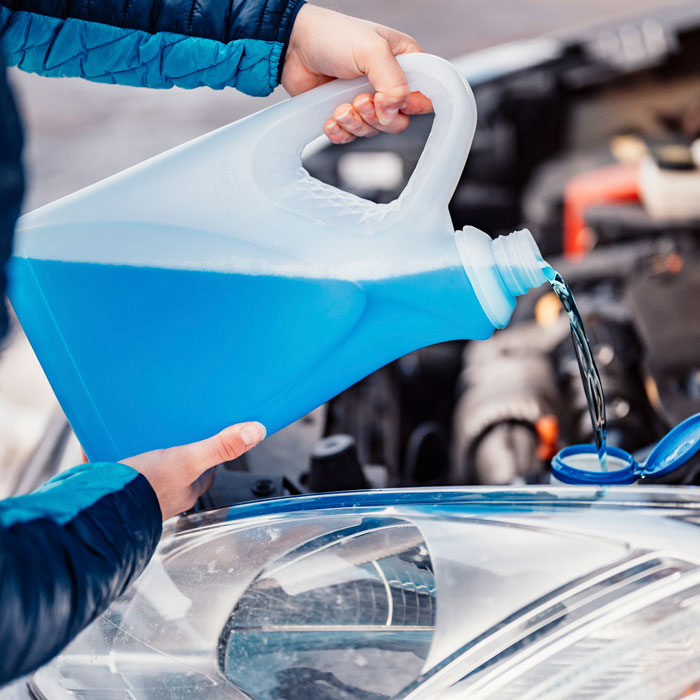 man pouring fluid into car