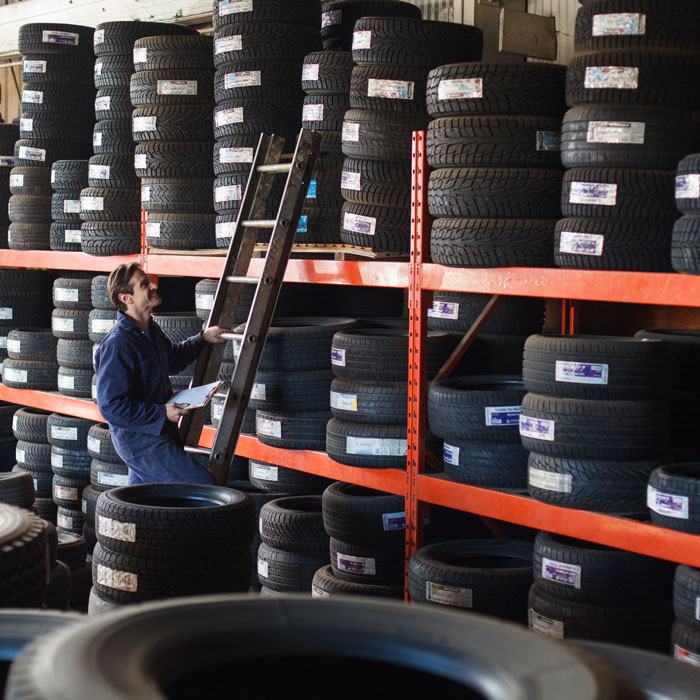 shelves lined with tires and worker climbing on ladder to view inventory